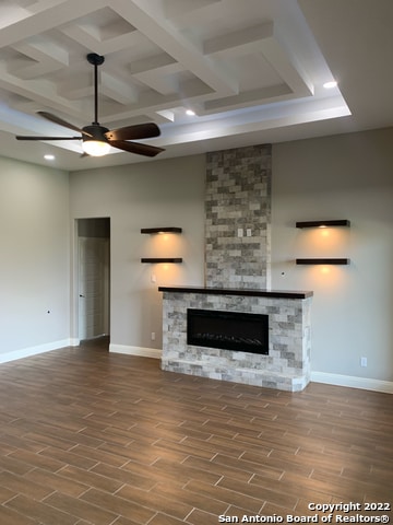 unfurnished living room with coffered ceiling, beamed ceiling, a stone fireplace, dark hardwood / wood-style floors, and ceiling fan