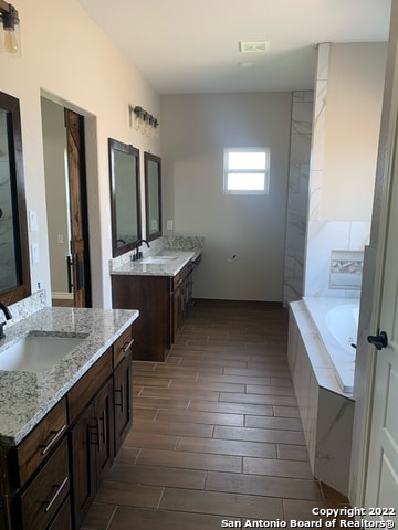 bathroom featuring double sink vanity and tiled tub