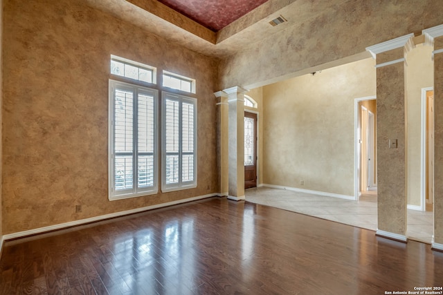 empty room featuring ornate columns, light wood-type flooring, a high ceiling, and plenty of natural light