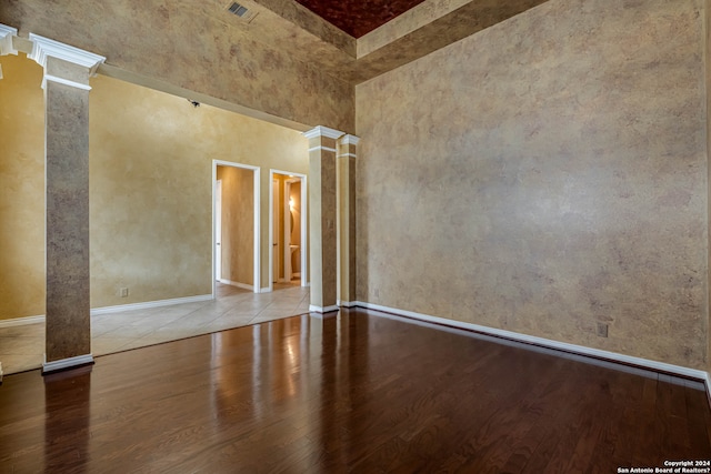 unfurnished room featuring a towering ceiling, decorative columns, and light wood-type flooring