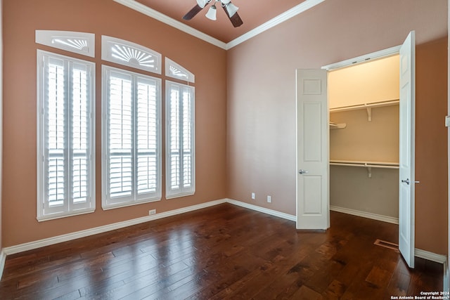 unfurnished bedroom with a closet, a walk in closet, ceiling fan, dark wood-type flooring, and crown molding