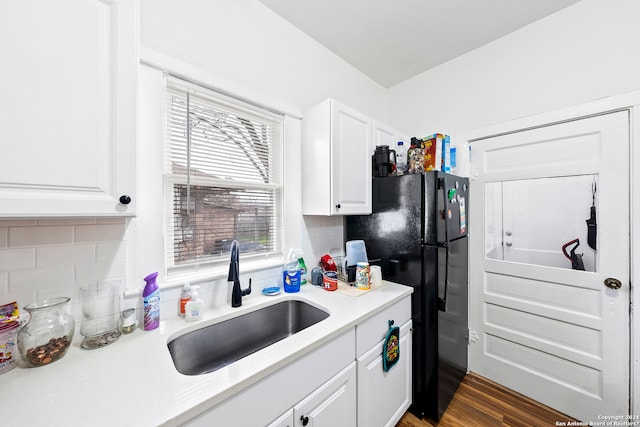 kitchen with black fridge, tasteful backsplash, white cabinets, dark hardwood / wood-style floors, and sink