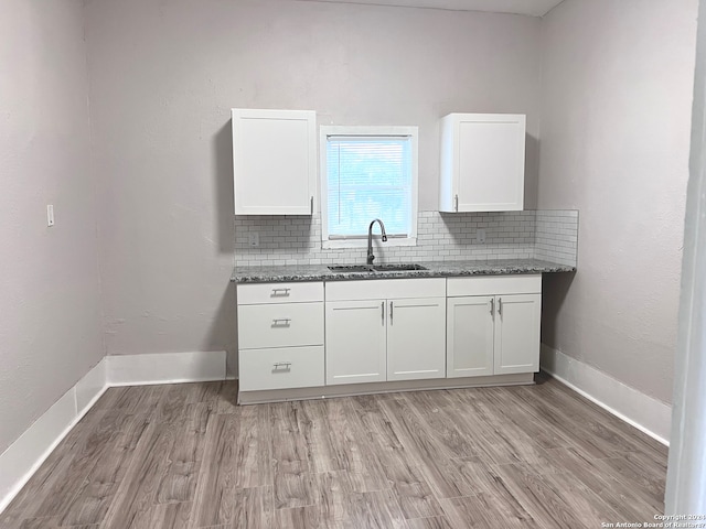 kitchen featuring tasteful backsplash, light hardwood / wood-style flooring, white cabinetry, dark stone countertops, and sink