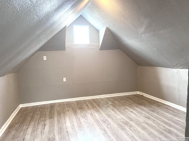 additional living space featuring lofted ceiling, hardwood / wood-style floors, and a textured ceiling