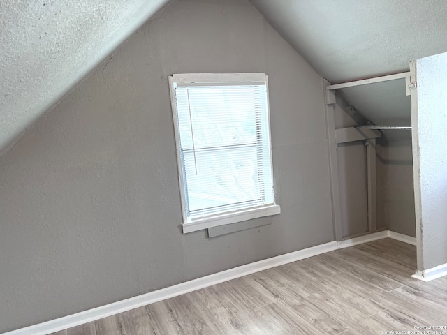 bonus room with vaulted ceiling, light hardwood / wood-style floors, and a textured ceiling