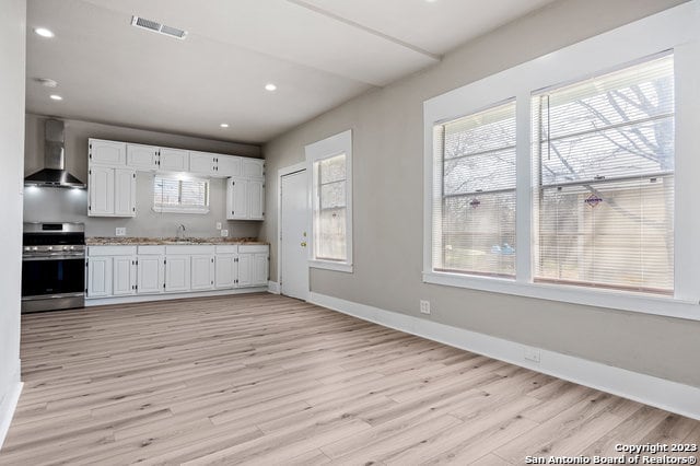 kitchen with white cabinetry, wall chimney exhaust hood, light hardwood / wood-style floors, and stove