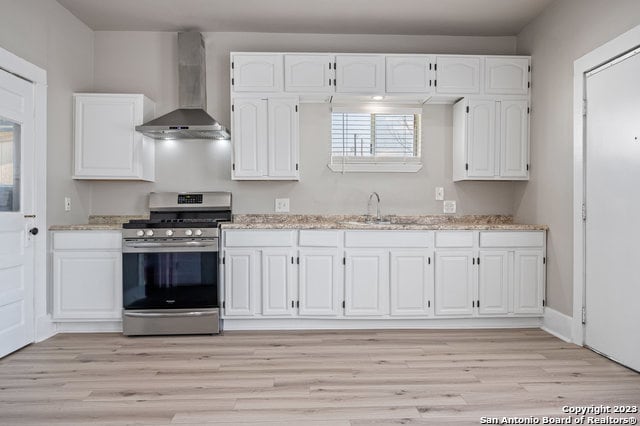 kitchen with light hardwood / wood-style floors, wall chimney range hood, white cabinetry, and stainless steel range