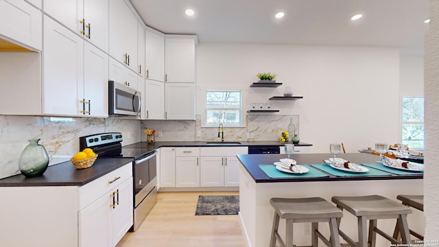 kitchen with sink, light hardwood / wood-style flooring, backsplash, stainless steel appliances, and white cabinetry