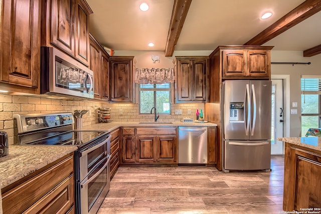 kitchen with appliances with stainless steel finishes, wood-type flooring, light stone countertops, sink, and beam ceiling