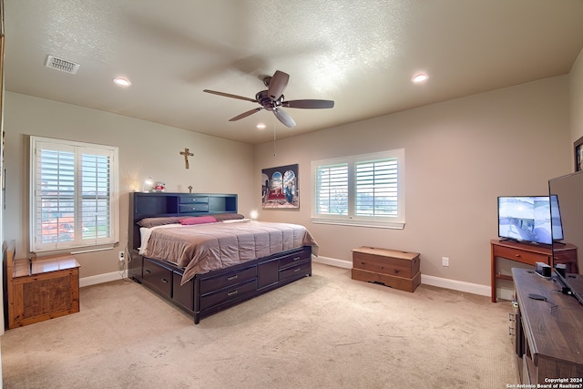 bedroom featuring ceiling fan, a textured ceiling, light colored carpet, and multiple windows