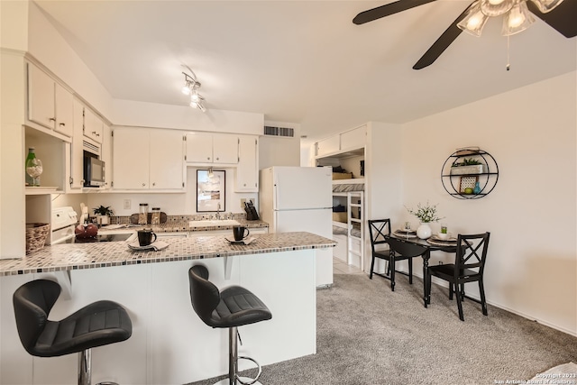 kitchen with kitchen peninsula, white appliances, light colored carpet, ceiling fan, and rail lighting