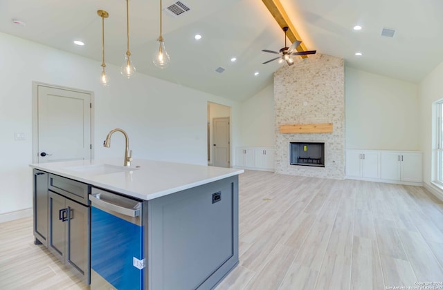 kitchen with an island with sink, ceiling fan, gray cabinetry, beam ceiling, and a stone fireplace