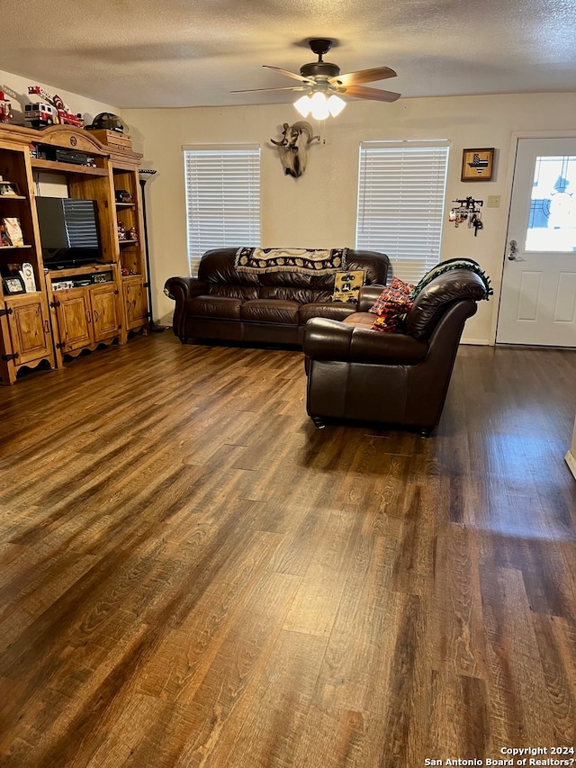 living room featuring dark hardwood / wood-style flooring, ceiling fan, and a textured ceiling