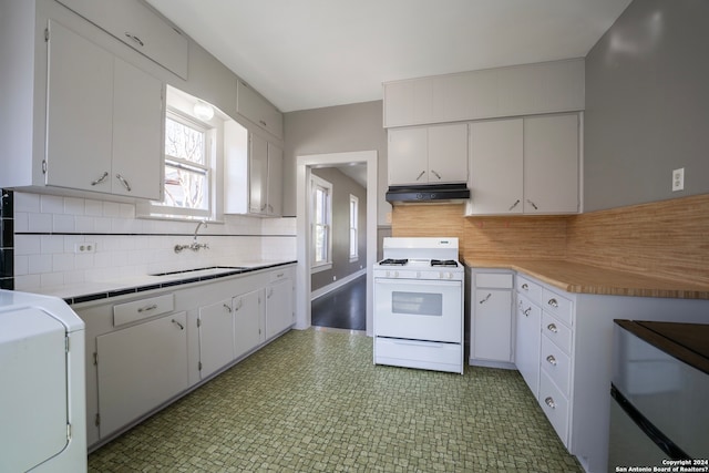 kitchen with dark tile floors, sink, white range with gas stovetop, white cabinets, and washer / dryer