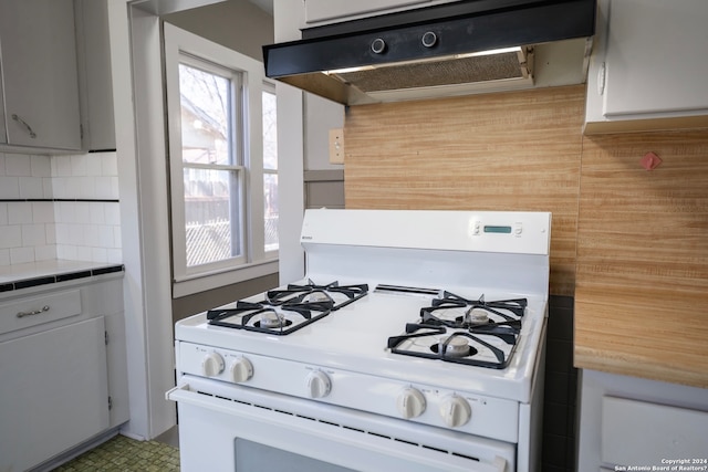 kitchen with gray cabinets, white gas range, backsplash, fume extractor, and tile floors