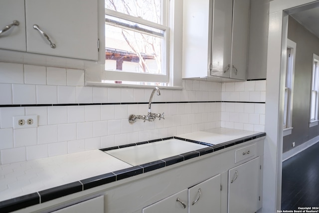 kitchen featuring backsplash, tile countertops, white cabinetry, and sink