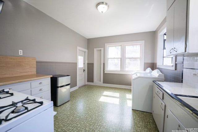 washroom with washer and clothes dryer, light tile flooring, and tile walls