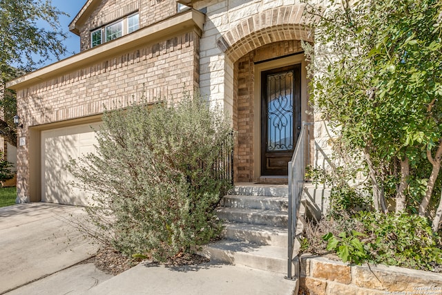 view of exterior entry with a garage, driveway, and brick siding