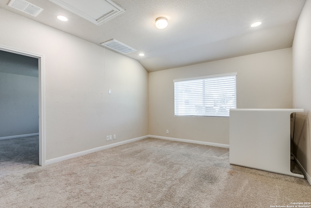 empty room featuring carpet floors, attic access, visible vents, and vaulted ceiling