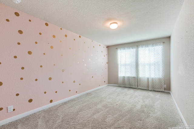 spare room with light carpet, a textured ceiling, baseboards, and wallpapered walls