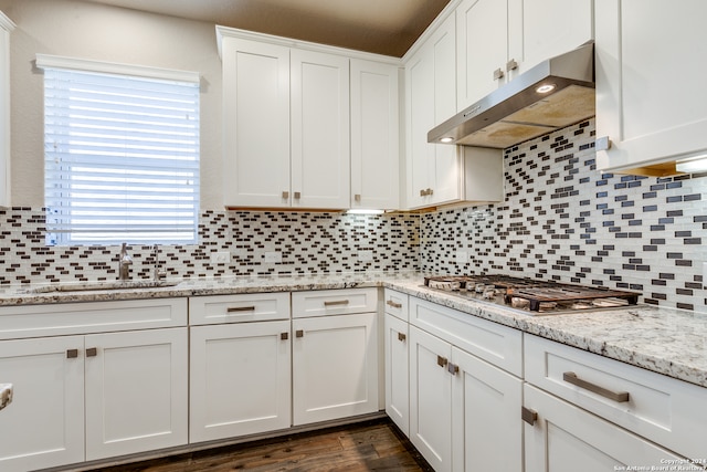 kitchen with white cabinets, a sink, stainless steel gas cooktop, backsplash, and exhaust hood