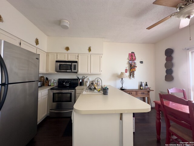 kitchen featuring appliances with stainless steel finishes, white cabinetry, dark hardwood / wood-style flooring, ceiling fan, and sink