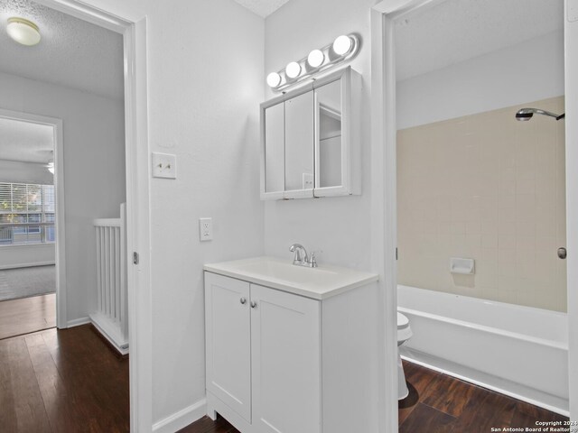 full bathroom with tiled shower / bath, vanity, wood-type flooring, a textured ceiling, and toilet