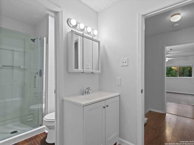 bathroom featuring vanity, a textured ceiling, wood-type flooring, a shower with door, and toilet