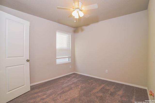 unfurnished room featuring ceiling fan, dark carpet, and a wealth of natural light