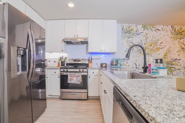 kitchen featuring appliances with stainless steel finishes, light stone counters, tasteful backsplash, light hardwood / wood-style floors, and white cabinetry