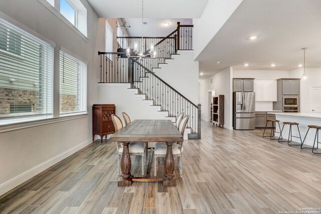 dining room featuring a high ceiling, a healthy amount of sunlight, a chandelier, and light wood-type flooring