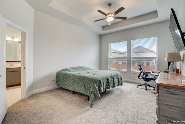 bedroom featuring light carpet, a tray ceiling, ceiling fan, and ensuite bathroom