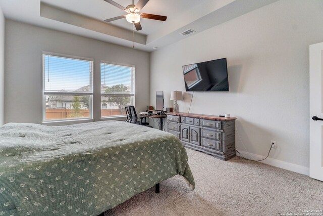 bedroom with a raised ceiling, ceiling fan, and light carpet