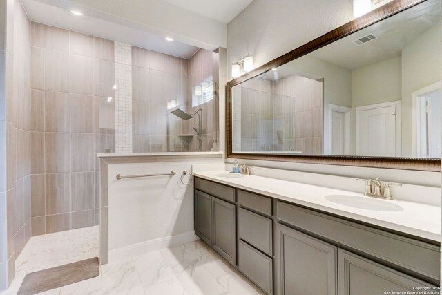 bathroom with tiled shower, double sink, tile flooring, and large vanity