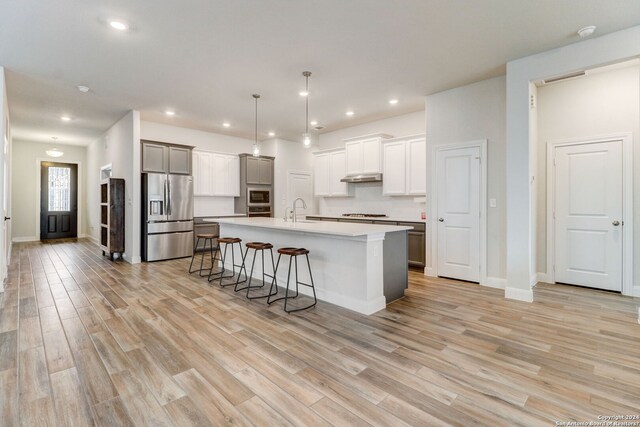 kitchen featuring appliances with stainless steel finishes, a kitchen bar, light wood-type flooring, and a center island with sink