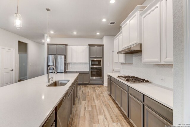 kitchen with decorative light fixtures, backsplash, sink, light hardwood / wood-style flooring, and stainless steel appliances