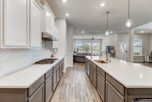 kitchen with an island with sink, sink, stainless steel appliances, tasteful backsplash, and white cabinetry