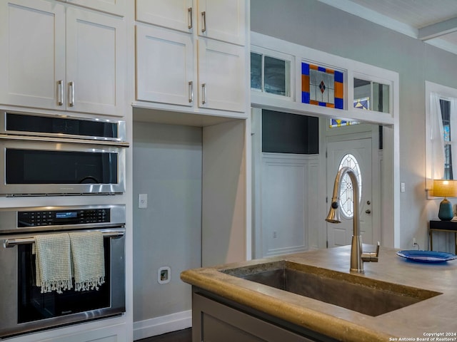 kitchen featuring white cabinetry, crown molding, double oven, and sink