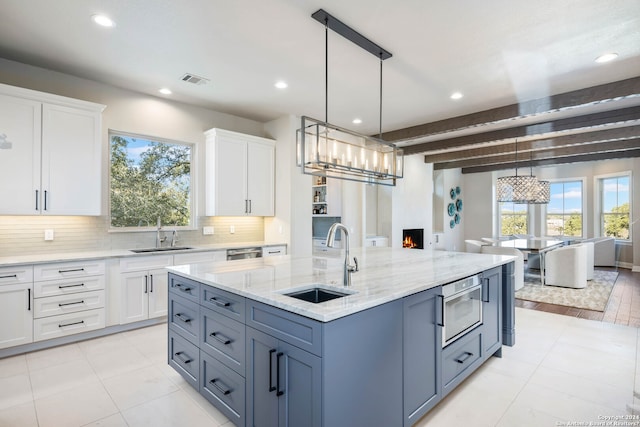 kitchen featuring light tile patterned floors, white cabinets, beamed ceiling, hanging light fixtures, and sink