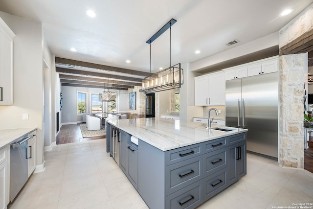 kitchen featuring beamed ceiling, light hardwood / wood-style flooring, a center island with sink, pendant lighting, and white cabinetry