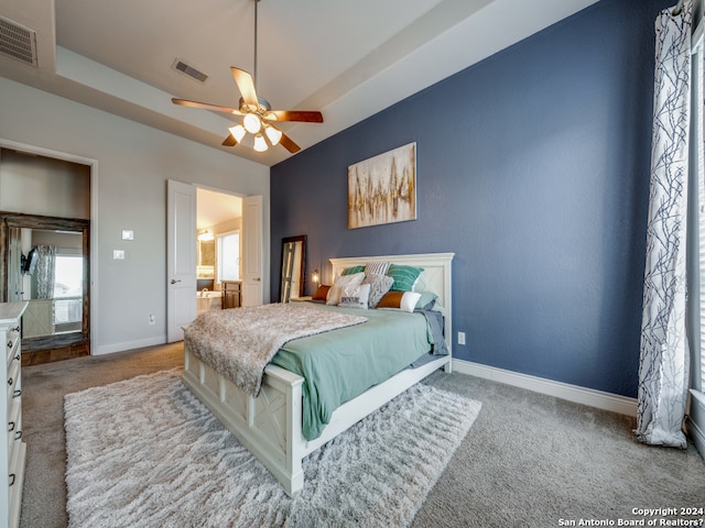 carpeted bedroom with a raised ceiling, ceiling fan, and ensuite bathroom