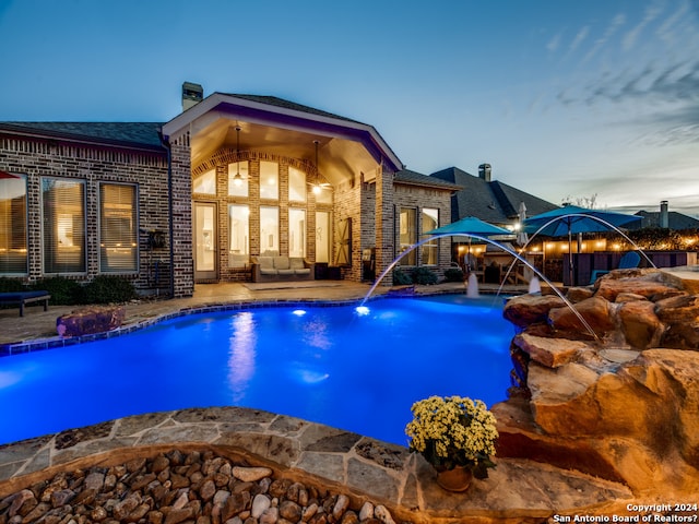 pool at dusk featuring pool water feature and a patio