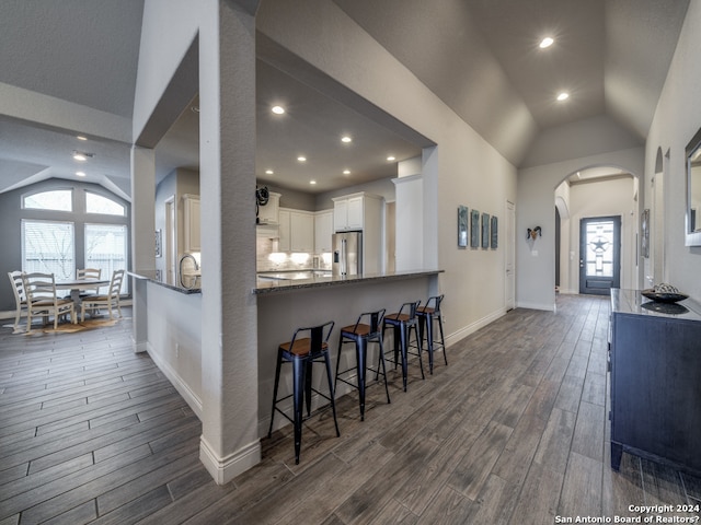 kitchen with high end fridge, dark wood-type flooring, white cabinetry, kitchen peninsula, and vaulted ceiling