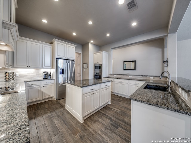 kitchen with a kitchen island, appliances with stainless steel finishes, dark stone counters, sink, and dark hardwood / wood-style flooring