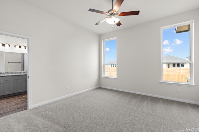 unfurnished bedroom featuring dark colored carpet, ensuite bathroom, and ceiling fan