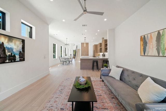 living room featuring light hardwood / wood-style flooring, a wealth of natural light, and ceiling fan with notable chandelier