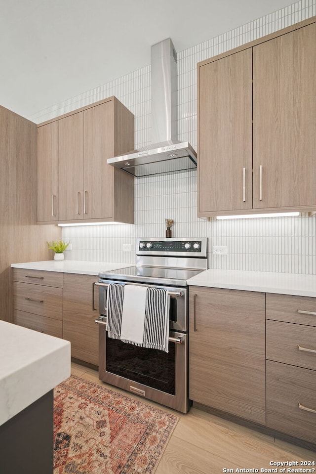 kitchen featuring range with two ovens, backsplash, light wood-type flooring, and wall chimney range hood