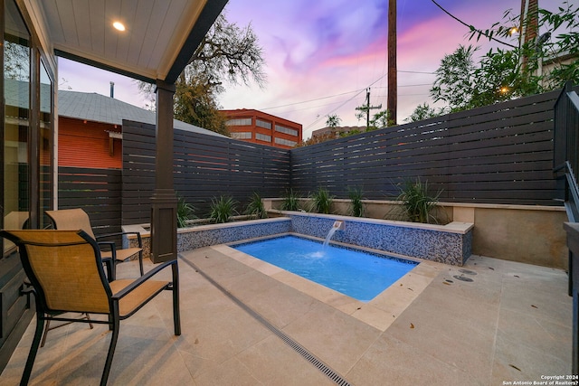 pool at dusk featuring a hot tub, pool water feature, and a patio