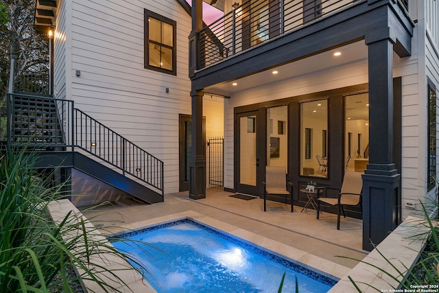 pool at dusk featuring a jacuzzi and a patio area