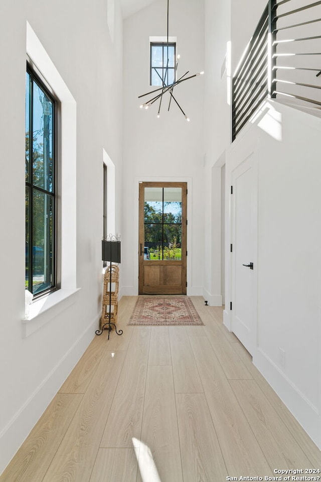 entrance foyer with a notable chandelier, light hardwood / wood-style floors, and a towering ceiling